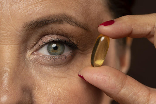 A close-up of a woman holding a yellow gel capsule near her eye, indicating a focus on eye care supplements. 