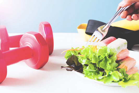 An image of a healthy meal with a plate of salad and a fork, accompanied by pink dumbbells and workout gear, symbolizing muscle health, calorie planning