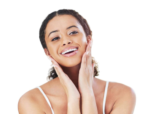 A woman smiling and gently touching her face, showcasing her skin's natural glow. 