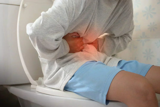 A person sitting on a toilet, holding their stomach in pain, with a red glow indicating discomfort, possibly from digestive issues.