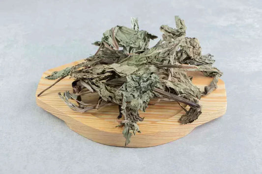 Dried Epimedium leaves displayed on a wooden cutting board, showcasing their green and brown color. The leaves are arranged loosely with a textured surface, indicative of the plant commonly known as Horny Goat Weed, highlighting its potential benefits.