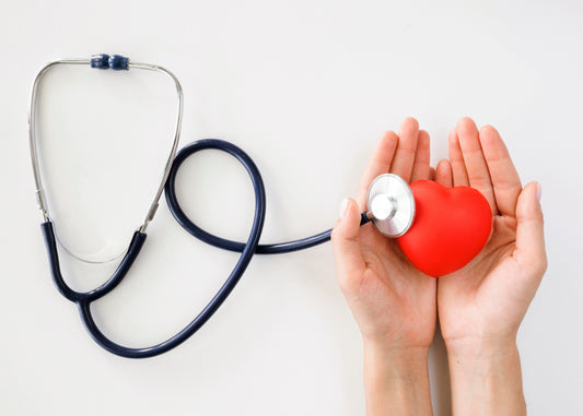 Two hands holding a red heart-shaped object while a stethoscope rests nearby, symbolizing heart health and medical care.