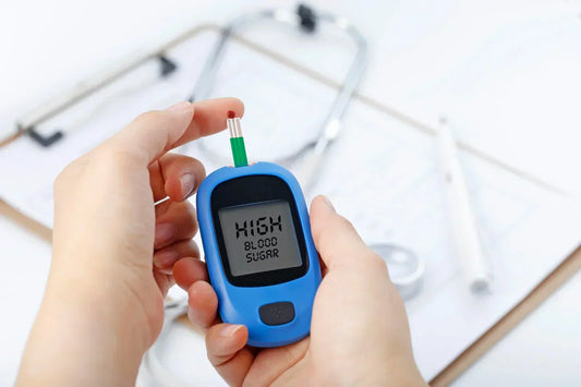 A person holding a glucose meter displaying a "HIGH BLOOD SUGAR" reading, with a stethoscope and medical tools in the background.
