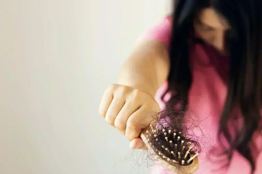 A woman holding a hairbrush with hair strands tangled in it, visibly frustrated by hair loss.