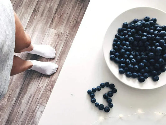 An image of a person wearing white socks standing near a plate of blueberries