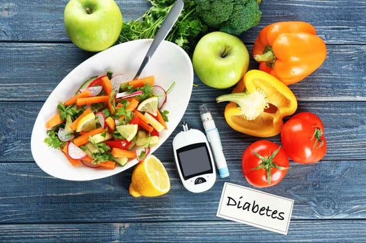 A colorful salad in a white bowl surrounded by fresh vegetables like bell peppers, tomatoes, and apples. A glucometer and insulin pen are placed nearby, with a label reading 'Diabetes' on a wooden surface.