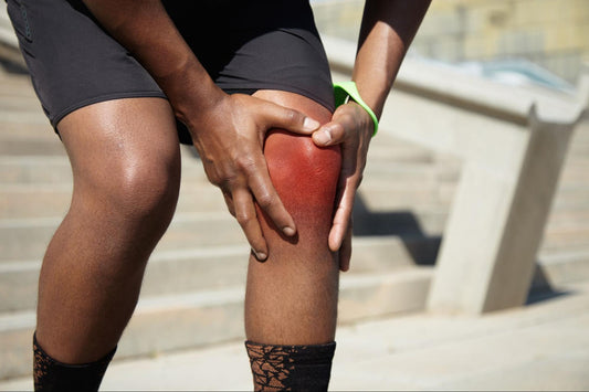 A person in athletic wear holding a swollen knee while standing on outdoor steps, indicating possible knee swelling and inflammation.