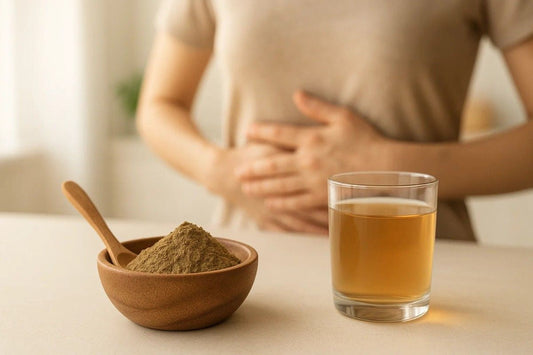 A person holding their stomach while sitting at a table with a bowl of brown powder and a glass of brown liquid, suggesting the use of Triphala for gas and bloating.