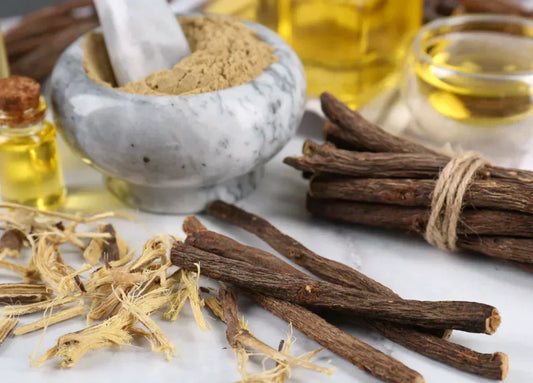 An image of licorice root sticks, dried pieces, and licorice powder in a marble mortar, along with bottles of oil in the background.