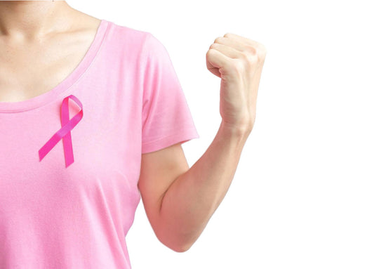 A person wearing a pink t-shirt with a pink ribbon pinned to it, showing a raised fist as a gesture of strength and support. This image relates to the theme of breast cancer awareness and how Holo Oncolis Helps Cancer Patients Regain Energy.