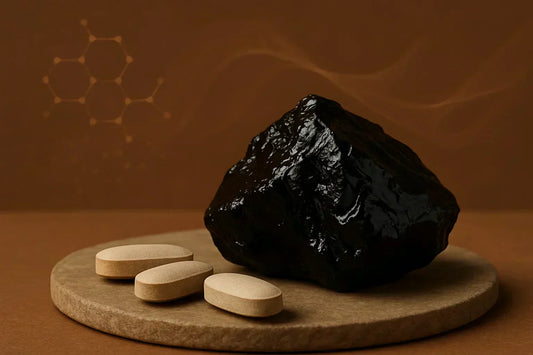 A dark, glossy chunk of Shilajit displayed alongside three beige sex boosting tablets on a circular wooden surface, with a brown background featuring abstract scientific patterns.