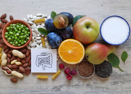 An assortment of healthy foods, including fruits, nuts, seeds, legumes, and pasta, with a drawing of the digestive system, emphasizing gut health and nutrition.